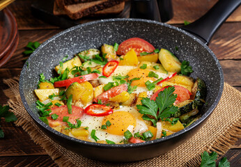 Fried eggs and potatoes, tomatoes, zucchini  and chili peppers on wooden table.