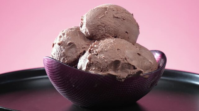 Balls of chocolate ice cream slowly rotate against a brightly colored background.
