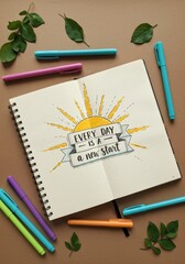 Motivational quote in notebook – Every day is a new start with colorful pens and leaves