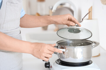 Woman and cooking pot with boiling water on mini stove in kitchen, closeup
