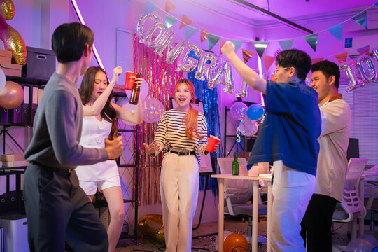 Happy office partners, men and women, joyfully celebrate Christmas and New Year together at a festive office party dancing, singing, drinking, laughing, and cheering in a warm, cheerful night of tea