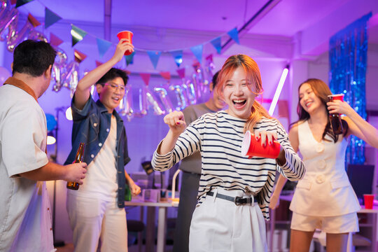 Happy office partners, men and women, joyfully celebrate Christmas and New Year together at a festive office party dancing, singing, drinking, laughing, and cheering in a warm, cheerful night of tea