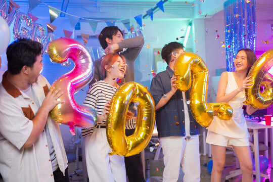 Business partners celebrate vibrant 2026 New Year office party with golden balloons, dancing, singing and confetti showers during festive nighttime celebration, sharing joyful moments and professional