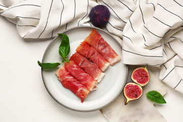 Plate with delicious prosciutto slices, basil leaves and fresh figs on white background
