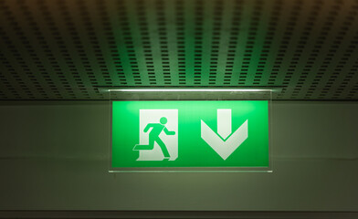 Signalisation de sortie d'urgence au plafond dans un couloir éclairé vert pour indiquer la direction.