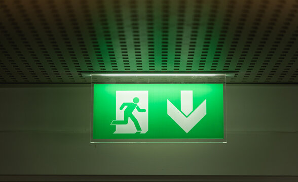 Signalisation de sortie d'urgence au plafond dans un couloir &eacute;clair&eacute; vert pour indiquer la direction.