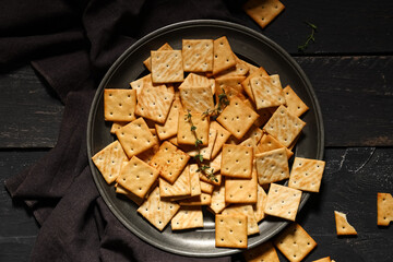 Composition with plate of tasty crackers on black wooden background, closeup