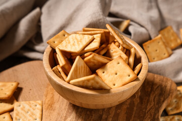 Composition with wooden bowl of tasty crackers on grey napkin as background, closeup