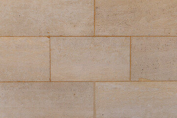 Mur en pierre beige avec des joints visibles, une structure solide et un aspect naturel sur fond clair.