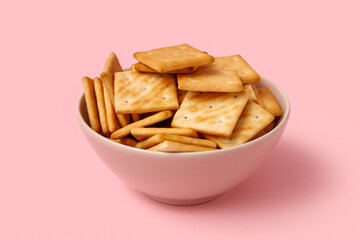 Bowl with tasty crackers on pink background, closeup