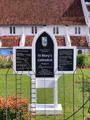 Obraz premium Anglican St Mary's Cathedral, in Kuala Lumpur, Malaysia. The historic church building with its distinctive tiled roof, white walls, and a prominent information sign on a green lawn