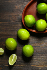 Plate with fresh ripe limes on wooden background