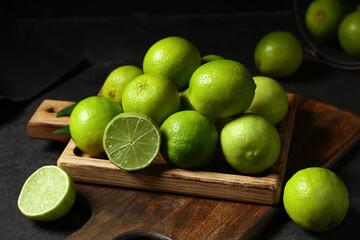 Wooden board with fresh ripe limes on black background