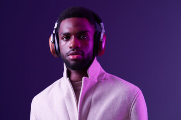 Stylish young Black man wearing headphones, featuring a modern light colored coat against a vibrant purple background, exuding confidence and contemporary style