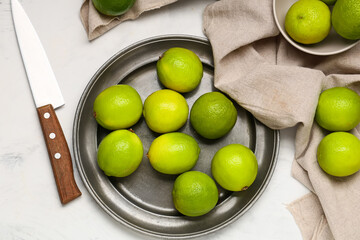 Plate with fresh ripe limes on white background