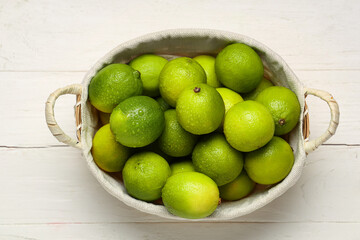 Wicker basket with fresh ripe limes on white wooden background
