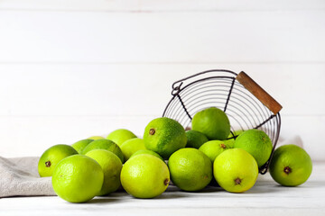 Basket with fresh ripe limes on white wooden background