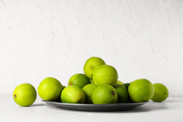 Plate with fresh ripe limes on white background