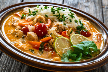 Tom Yum soup - Thai soup with chicken breast nuggets, vegetables and rice noodles on wooden table	
