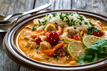 Tom Yum soup - Thai soup with chicken breast nuggets, vegetables and rice noodles on wooden table	
