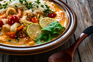 Tom Yum soup - Thai soup with chicken breast nuggets, vegetables and rice noodles on wooden table	
