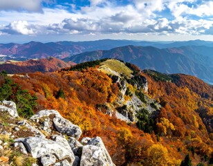Fototapeta premium Vivid autumn foliage covers mountain ridges under a partly cloudy sky