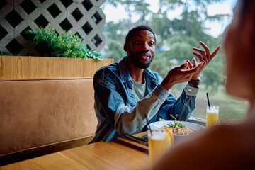 African American man actively talking and gesturing to a woman during a conversation at a modern restaurant
