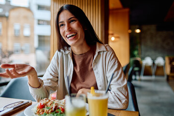 Young woman laughing and chatting over a casual lunch in a bright cafe, enjoying salad and juice...