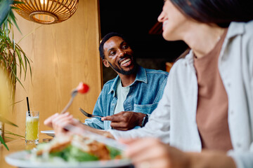 Happy diverse couple eating healthy food and fresh juice in a cafe, enjoying a pleasant lunch together