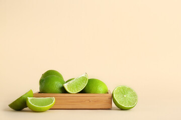 Wooden box with fresh ripe limes on beige background
