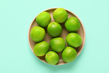 Plate with fresh ripe limes on turquoise background