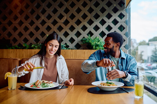 Diverse couple enjoying lunch and adding dressing to their meals in a casual, contemporary restaurant setting, smiling and chatting