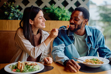 Happy young couple enjoying dinner together at a restaurant, laughing while feeding each other during an intimate date