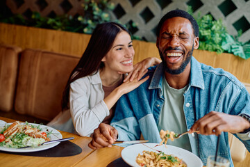 Happy diverse couple having fun together, laughing while enjoying a meal at a restaurant, celebrating love and connection