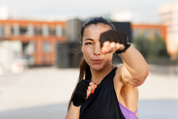 Young female practicing punches outdoors, wearing gloves. Portrait of a young woman during an intense warm-up.