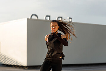 Young female in black fitness attire practicing an intense workout. Woman with long hair jumping...