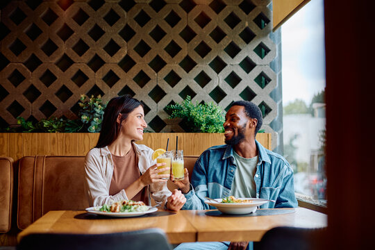 Diverse couple enjoying a pleasant date at a restaurant, toasting with drinks and smiling happily during their dinner - Powered by Adobe