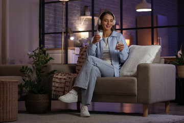 Obraz premium Young woman with headphones and glass of milk using mobile phone at home late in evening