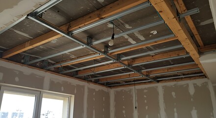 Exposed metal ceiling grid installed beneath a wooden subfloor in an unfinished room with light-gray drywall.
