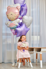 Cute little child girl in pink dress with flowers and pink purple balloons. Birthday concept.