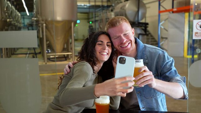 Young couple taking selfie while drinking beer at brewery