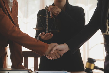 Lawyer shaking hands with a client making about documents, contracts, agreements, cooperation agreements with a female client at the lawyer's desk and a hammer at the table.