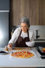 Senior woman preparing homemade pizza in bright kitchen