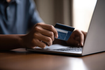 Person holding credit card near laptop making secure online payment digital transaction internet shopping e commerce modern technology financial security home environment close up