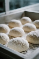 Fototapeta premium Close-up of multiple round pizza dough portions resting on a floured surface in a tray inside a kitchen with soft natural lighting coming from a nearby window