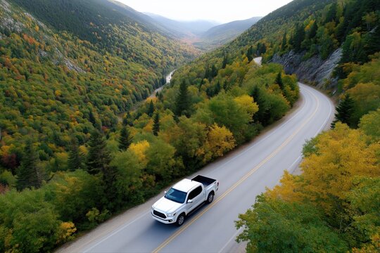 White pickup truck navigating scenic road through vibrant autumn forest landscape