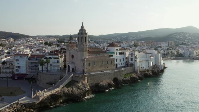 Aerial view of the Church of Sant Bartomeu i Santa Tecla with the town and mountains in the background, Sitges, Barcelona, Spain.