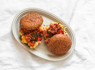 Breakfast, brunch burgers with scrambled eggs, pickled cucumbers mustard, mayonnaise sauce, tomatoes and bacon on a light background, top view