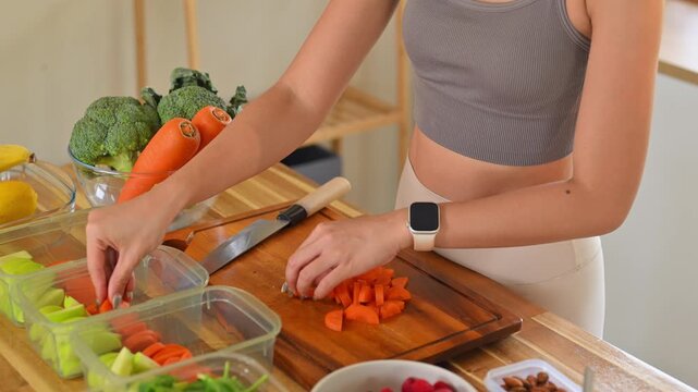 Young woman slicing fresh carrots and preparing ingredients for weekly healthy meal prep at home