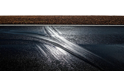 Tire tracks streak across wet asphalt below a field. Dark, moody, contrasting light